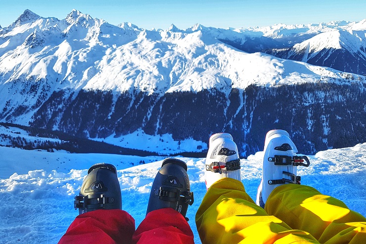 Picture of skiers boots while resting in the snow admiring the view of the snow covered mountains - Skiing in Davos Ski Resort